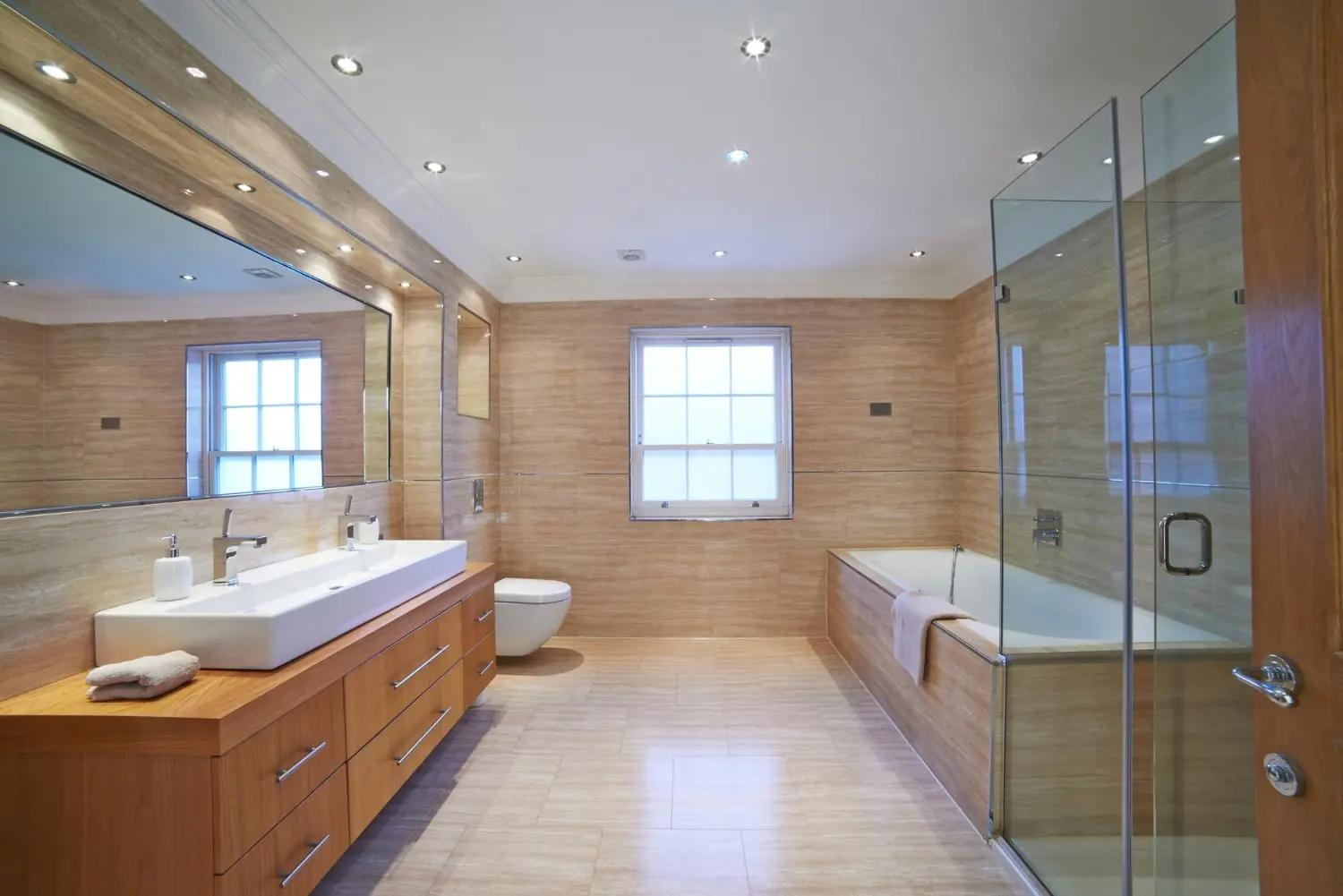 Completed warm bathroom remodel with wood double vanity and glass shower